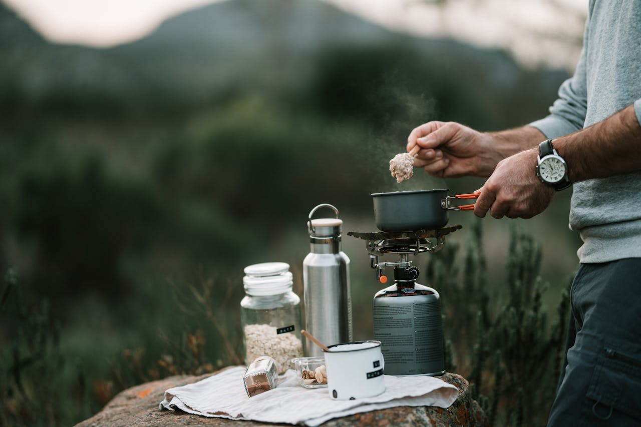 Person cooking oatmeal on portable stove in outdoor campsite setting, emphasizing adventure and nature.